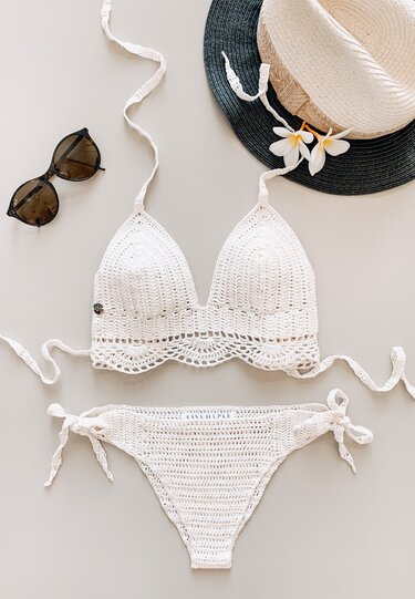 Weißer gehäkelter Bikini mit Strohhut und Sonnenbrille auf hellem Hintergrund