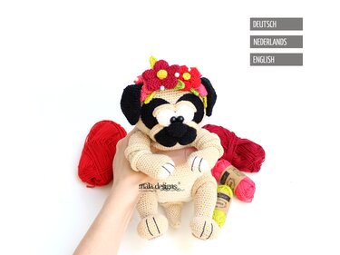 Gehäkelter Mops mit Blumenkranz, in der Hand gehalten; Wollknäuel im Hintergrund
