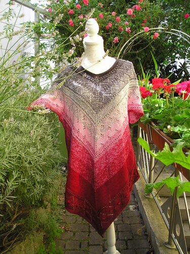 Mannequin mit gestrickter Tunika, Farbverlauf Grau–Rosa–Dunkelrot, V‑Form, Ajourmuster, kurze Ärmel, präsentiert im Garten