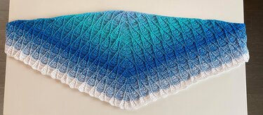 Flach ausgelegtes gehäkeltes Dreieckstuch in Türkis-, Blau- und Weißtönen mit Muschelmuster