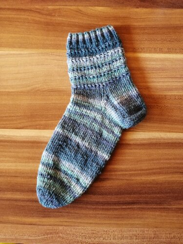 Gestrickte Socke mit Rippbündchen, Ferse und meliertem Garn auf Holzuntergrund