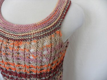 Nahaufnahme eines gestrickten Tops mit kraus-rechts Bündchen, Lochmuster und mehrfarbigen Streifen.