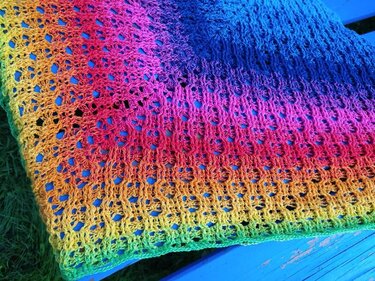Gehäkeltes Dreieckstuch in Regenbogenfarben mit Lochmuster auf blauem Untergrund