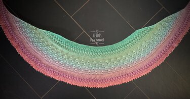 Halbrundes gehäkeltes Tuch mit Farbverlauf in Rosa, Lila, Blau und Grün auf dunklem Hintergrund.