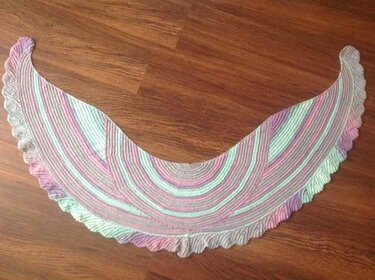 Gestricktes Halbrundtuch in Pastellstreifen mit gewellter Kante auf Holzboden.