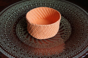 Gehäkelter runder Korb in Pfirsichfarbe auf einem gemusterten Tablett