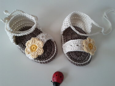 Gehäkelte Babysandalen mit Riemen, Bindebändern und pastellgelber Blüte auf hellem Untergrund