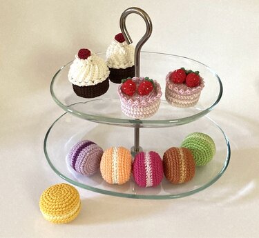 Gehäkelte Süßigkeiten auf einer Etagere: Cupcakes, kleine Törtchen und bunte Makronen.