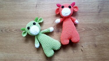 Nahaufnahme von zwei Amigurumi in Grün und Koralle mit sichtbaren Maschen, Ohren und geteilten Beinen