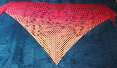 Gehäkeltes Dreieckstuch im Filetmuster mit Herzmotiv und Farbverlauf von Pink zu Orange auf blauem Hintergrund