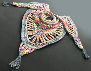 Multicolored crocheted triangle shawl with openwork details and tassels laid flat on a dark surface