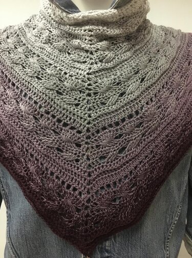 Hand-crocheted triangle shawl with grey-to-purple ombre, alternating textured bands and openwork stitches, draped on a mannequin.