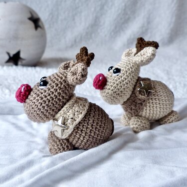 Zwei gehäkelte Rentier-Amigurumi in Beige und Braun mit roter Nase und Sternanhänger