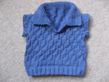Blauer gestrickter Kinderpullover mit Kragen und Zopfmuster auf hellem Teppich