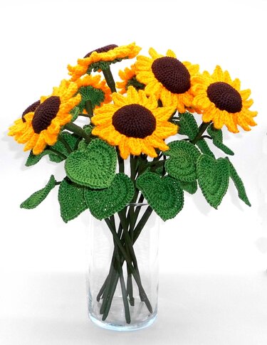 Crocheted sunflowers with yellow petals and brown centers in a clear glass vase