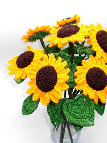Bouquet of yellow and brown crocheted sunflowers with green leaves in a clear glass vase.