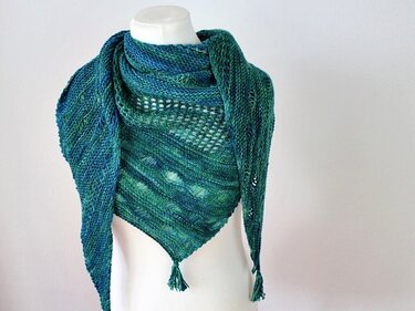 Gestricktes Dreieckstuch in blau-grünen Farbtönen mit Lochmuster und Quasten an einer Schaufensterpuppe