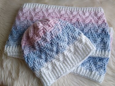 Gehäkelte Mütze und passender Loop in Weiß, Rosa und Hellblau auf hellem Felluntergrund