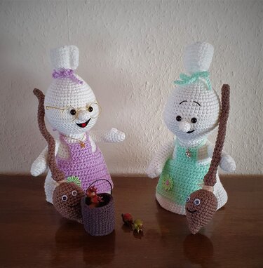 Zwei handgehäkelte Amigurumi-Hexen mit Schürzen, Brille, kleinen Besen und Körbchen