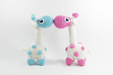 Zwei gehäkelte Amigurumi-Giraffen in Hellblau und Rosa mit den Köpfen aneinander