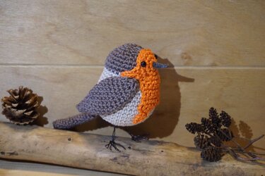 Gehäkelter Amigurumi‑Vogel mit orangefarbener Brust und Drahtbeinen