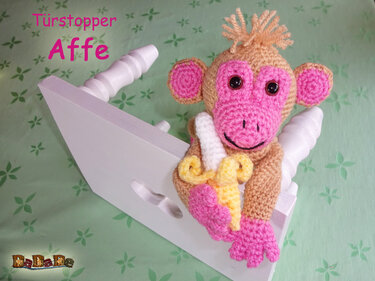 Gehäkelter Affe-Türstopper mit rosa Gesicht und gelber Banane auf weißem Türkeil