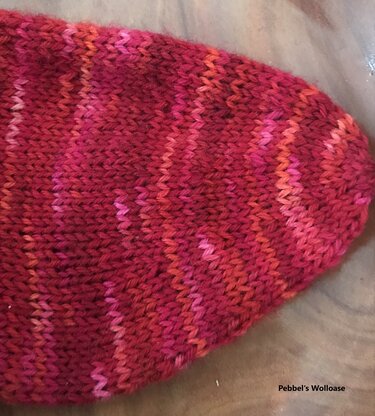 Gestrickte Sockenspitze in Rot-, Orange- und Pinktönen mit meliertem Streifenmuster auf Holzuntergrund.