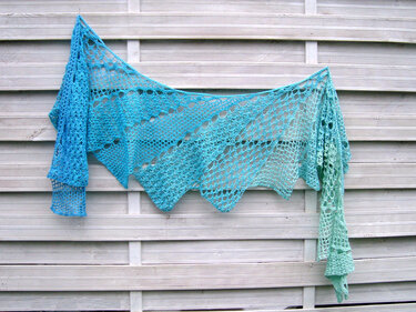 Türkis-blaues gehäkeltes Dreieckstuch mit Lochmuster, aufgehängt an einem weißen Lattenzaun