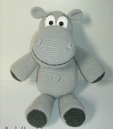 Sitzendes gehäkeltes graues Nilpferd-Amigurumi mit weißen Augen und dunklen Pfoten