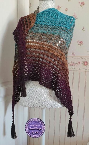 Gehäkeltes Dreieckstuch auf Schneiderpuppe, Farbverlauf Türkis–Braun–Violett, offenes Muster und Quasten.