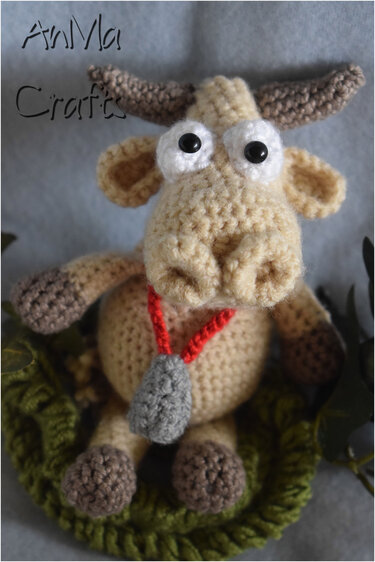 Beige gehäkelte Amigurumi-Kuh mit braunen Hörnern, großen Augen und roter Kordel