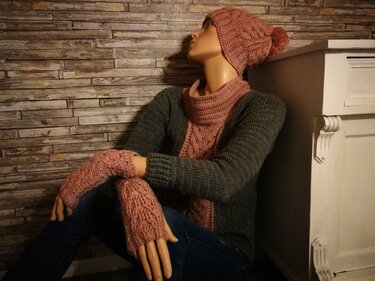 Gehäkelte rosafarbene Mütze mit Bommel, Schal und Fingerstulpen an einer Schaufensterpuppe