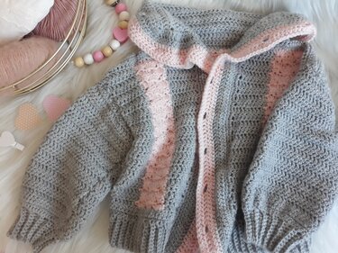 Gehäkelte graue Babyjacke mit rosa Blende und Kapuze, liegend