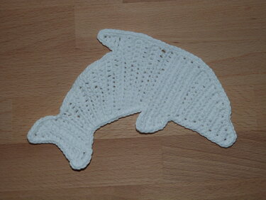 Weiße handgehäkelte Delfin-Applikation auf Holzuntergrund.
