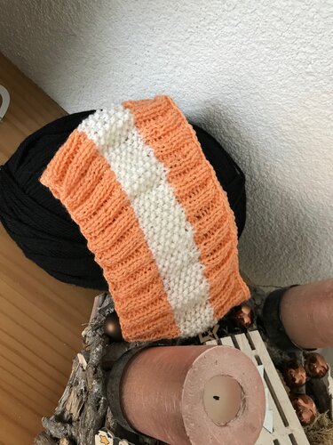 Orange-weiß gestreiftes gestricktes Stirnband mit Rippen- und Kraus-rechts-Muster auf schwarzem Wollknäuel