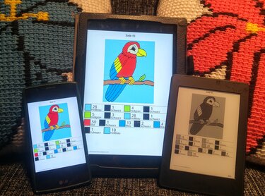 Drei Geräte zeigen Pixelhäkel-Charts eines Papageien mit Farblegenden; gehäkelte Decken im Hintergrund