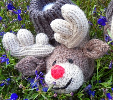 Handgefertigter Rentier-Babyschuh mit roter Pompon-Nase auf grünen Blättern und blauen Blüten