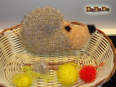 Gehäkelter Igel aus goldbraunem Effektgarn im Weidenkorb mit gelben und roten Pompons