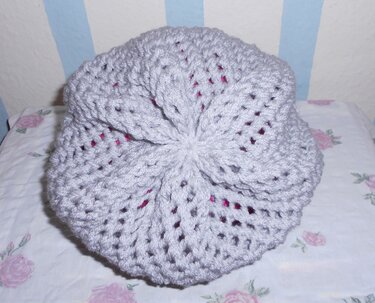 Hellgraue Strickmütze mit Lochmuster und fuchsiafarbenem Innenfutter auf gemustertem Stoff