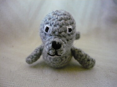 Gehäkelte graue Amigurumi-Robbe mit gestickter Nase und Augen auf hellem Hintergrund