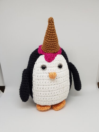 Gehäkelter Amigurumi-Pinguin, weißer Bauch, schwarze Flügel, orangefarbener Schnabel und Füße, braunes Horn mit pinker Basis