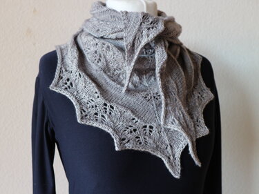 Gray triangle knitted shawl with lace motifs and scalloped border on a mannequin