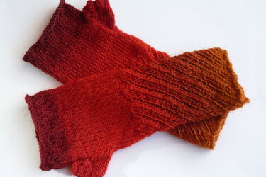 Gestrickte fingerlose Armstulpen in Rot‑Orange auf weißem Hintergrund