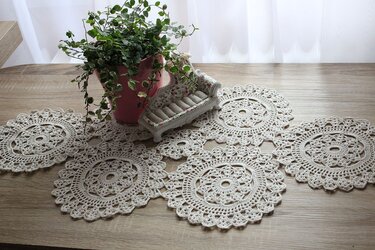 Handmade crochet lace doily table runner on a wooden surface with a potted plant and a decorative miniature sofa.