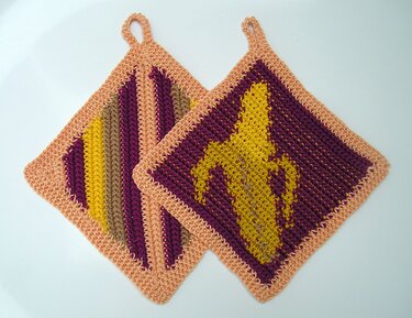 Zwei quadratische gehäkelte Topflappen, einer mit gelbem Bananenmotiv auf violettem Grund, einer gestreift, beide mit pfirsichfarbener Umrandung und Schlaufe