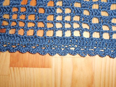 Blaues gehäkeltes Netzmuster mit wellenförmigem Muschelsaum auf Holz