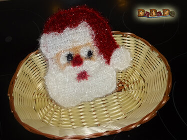 Gehäkelter Weihnachtsmann-Kopf mit roter Glitzermütze in hellem Flechtkorb
