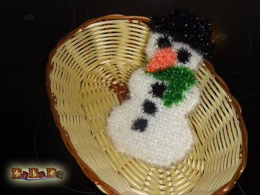 Gehäkelter Schneemann mit Hut und grünem Schal in einem Weidenkorb