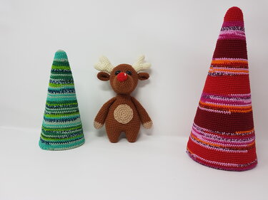Gehäkeltes Rentier-Amigurumi mit roter Nase zwischen zwei gestreiften Häkelkegeln