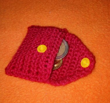 Rotes gehäkeltes Münztäschchen mit gelben Druckknöpfen und sichtbaren Münzen auf orangefarbener Fläche